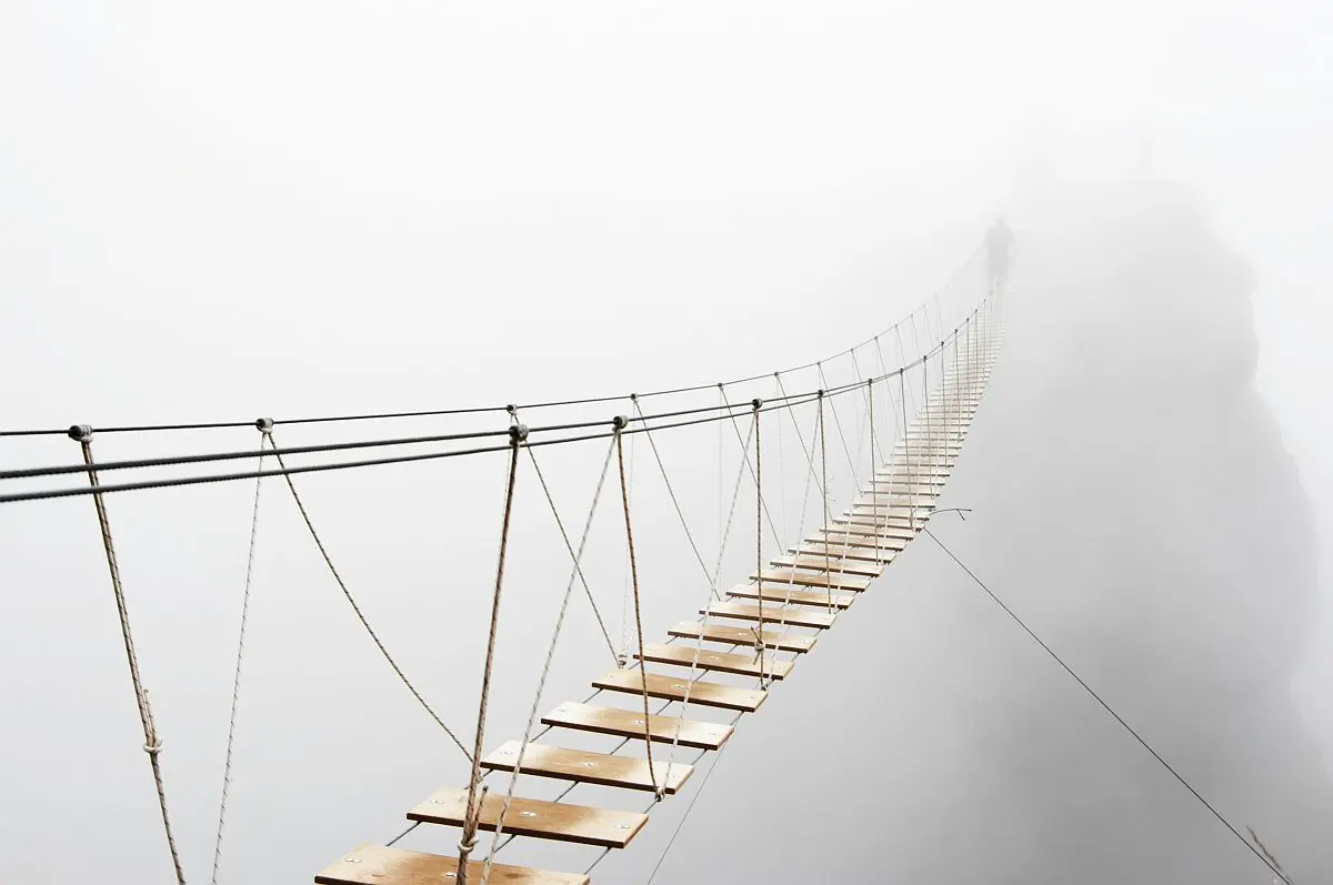 Risk and uncertainty concept: Fuzzy figure of man walking on hanging bridge disappearing into the distance in fog